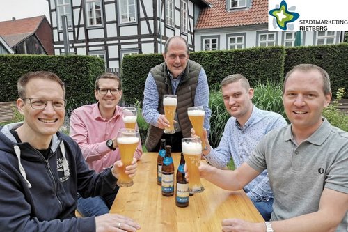 Vertreter des Vereins "Lebendiges Rietberg" und zwei Gastwirte sitzen im Drostengarten an einer Bierzeltgarnitur und stoßen mit einem Weizenbier an.