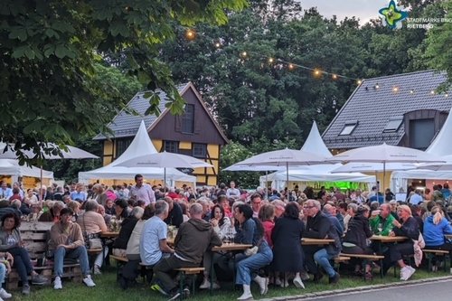 Blick aufs Weinfest 2024 mit vielen Menschen, die an Bierzeltgarnituren sitzen. Im Hintergrund die Pagoden-Zelte.
