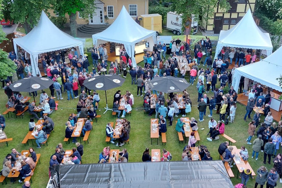 Aufsicht auf das Weinfest auf Gut Rietberg. Im Vordergrund eine Wiese, auf der Gäste an  Bierzeltgarnituren sitzen, im Hintergrund mehrere Pagodenzelte.
