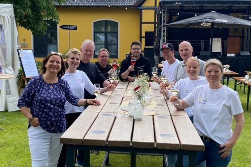 Die Weinhändler stehen auf Gut Rietberg um einen großen Tisch und halten Weingläser in ihren Händen.