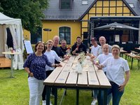 Die Weinhändler stehen auf Gut Rietberg um einen großen Tisch und halten Weingläser in ihren Händen.