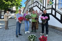 Vertreter von Stadtmarketing und Blumenexperten stehen vor dem Rathaus. Jeder hat einen Blumentopf mit einer blühenden Pflanze in der Hand.