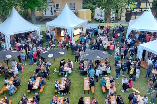 Aufsicht auf das Weinfest. Man sieht Bierzeltgarnituren, an denen Menschen sitzen, und Pagodenzelte im Hintergrund.