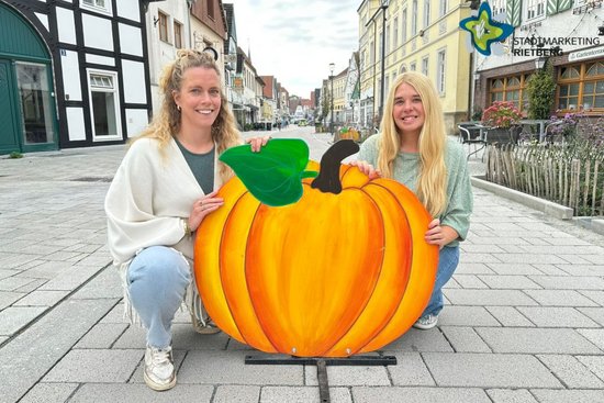 Laura Hunke (links) und Bianca Piekatz hocken auf der Fahrbahn der sanierten Rathausstraße, zwischen sich einen großen Deko-Kürbis aus Holz.