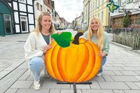 Laura Hunke (links) und Bianca Piekatz hocken auf der Fahrbahn der sanierten Rathausstraße, zwischen sich einen großen Deko-Kürbis aus Holz.