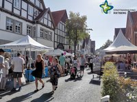 Viele Menschen spazieren bei Sonnenschein durch eine gut besuchte Straße.