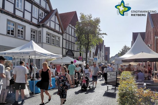Viele Menschen spazieren bei Sonnenschein durch eine gut besuchte Straße.