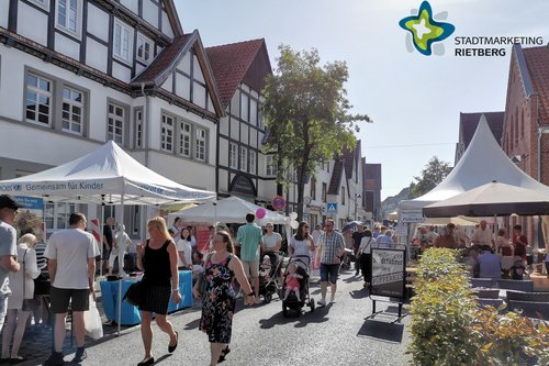 Viele Menschen spazieren bei Sonnenschein durch eine gut besuchte Straße.