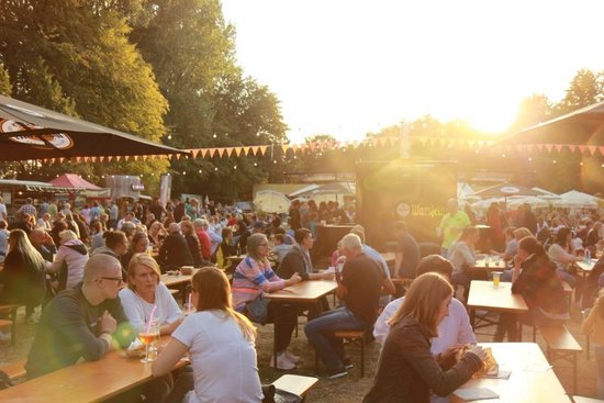Menschen sitzen in einem Biergarten an Bierzeltgarnituren, essen, trinken und unterhalten sich.