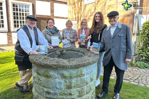 Gästeführer und Mitarbeiterinnen der Touristikinformation stehen am Brunnen im Garten des Heimathauses.