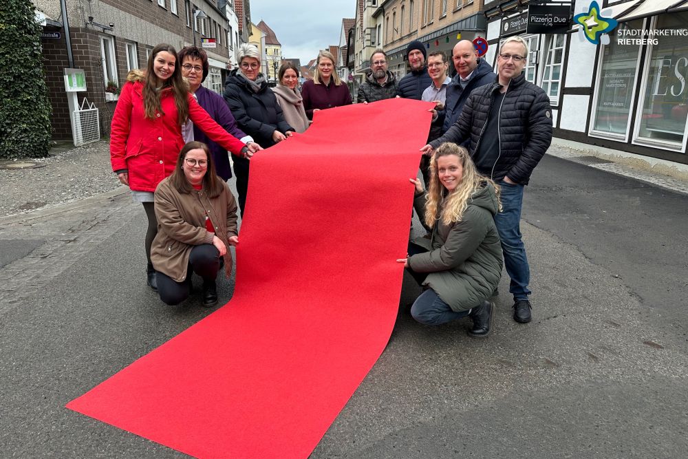 Händler, Gastronomen, Organisatoren und Sponsor stehen auf der Rathausstraße und halten einen ausgerollten roten Teppich in der Hand.