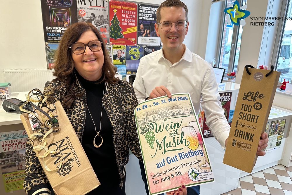 Sabine Kovar und Johannes Wiethoff vom Stadtmarketing halten ein Weinfest-Plakat und Weinpräsente in Händen.